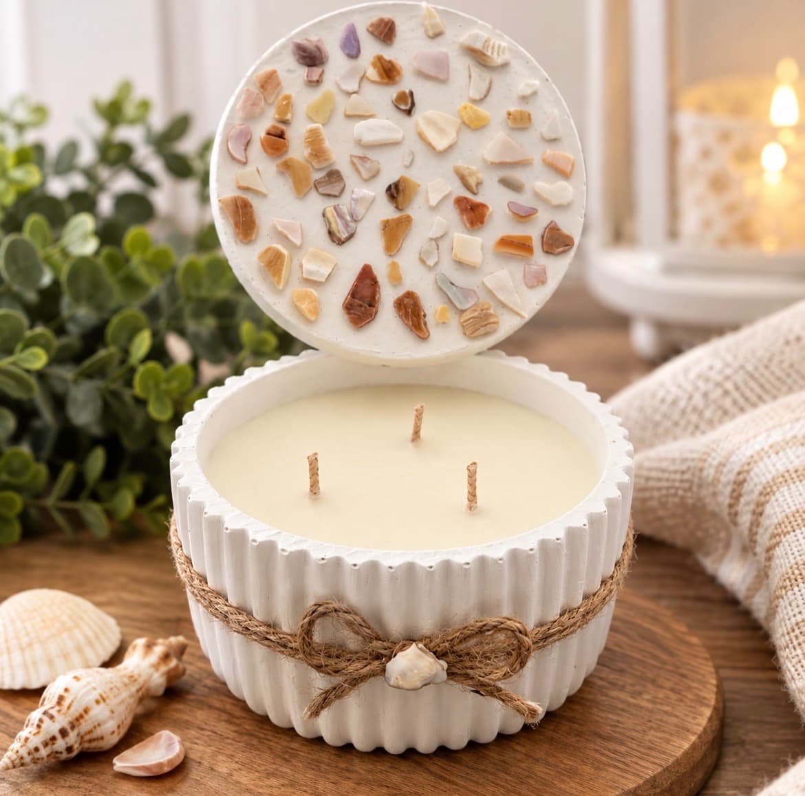 Three-wick candle in a white fluted vessel tied with twine, its round lid set above and inlaid with pieces of shell