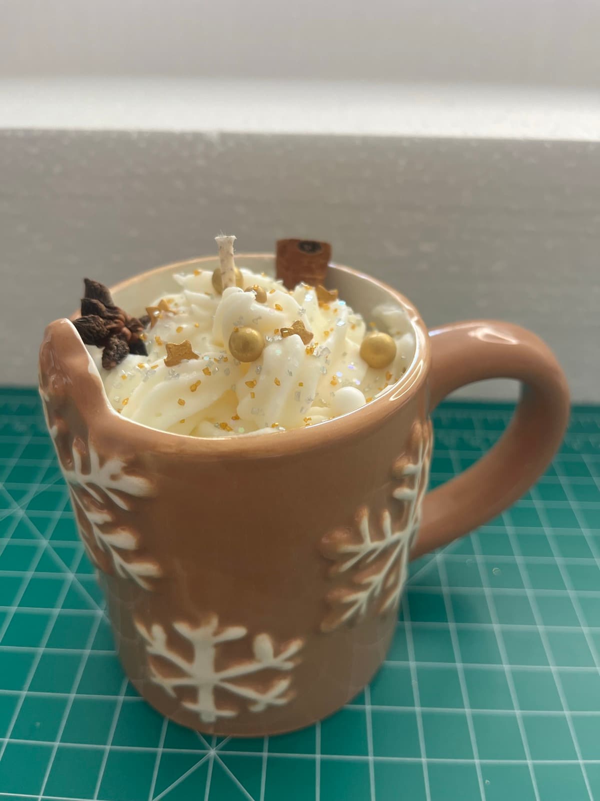 Ceramic mug candle with raised white snowflakes, topped with piped whipped-cream wax, gold beads and star anise